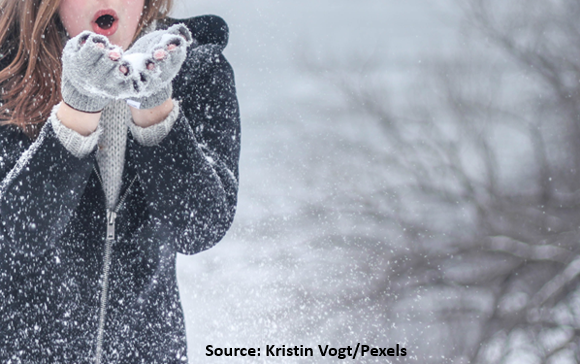 A woman blows snow from the palms of her gloved hands as she immerses herself in a snowy landscape. 